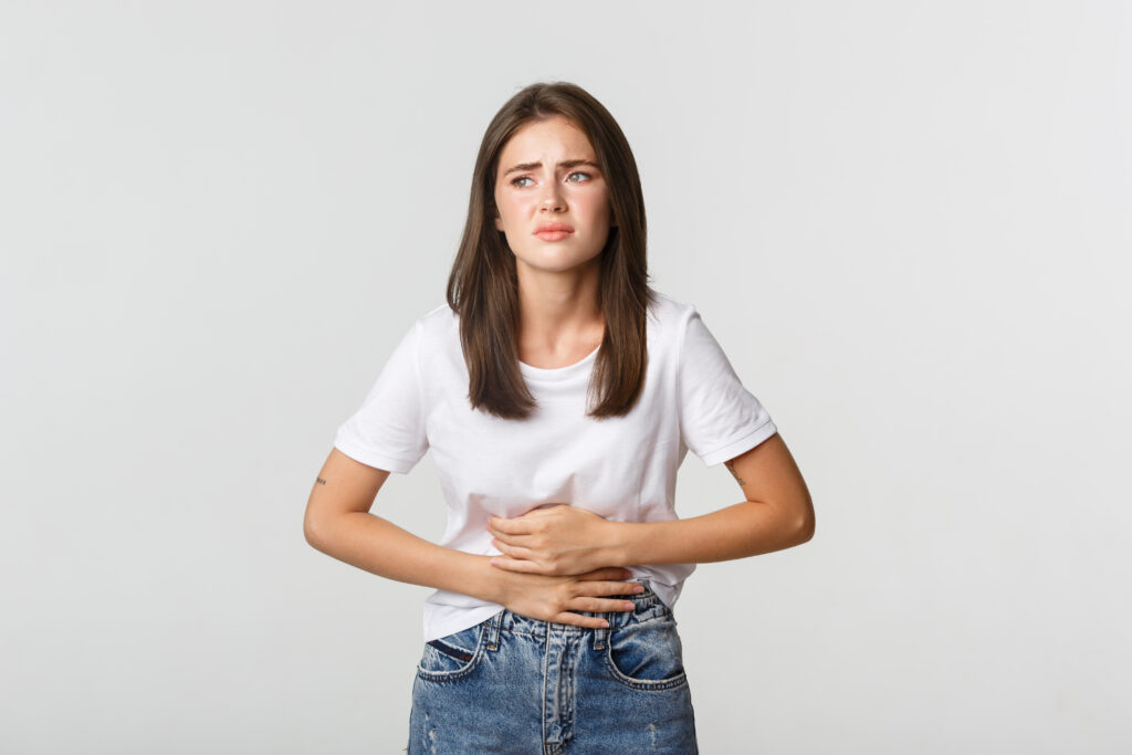 Mulher com dor de barriga segurando o abdômen, ilustrando sintomas de dor abdominal.